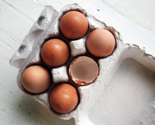 Packung mit fünf ganzen Eiern und einer aufgeschlagenen Schale